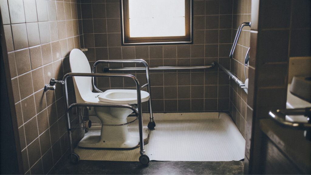 Baño adaptado con barras de apoyo, alfombrillas antideslizantes y asiento de ducha.